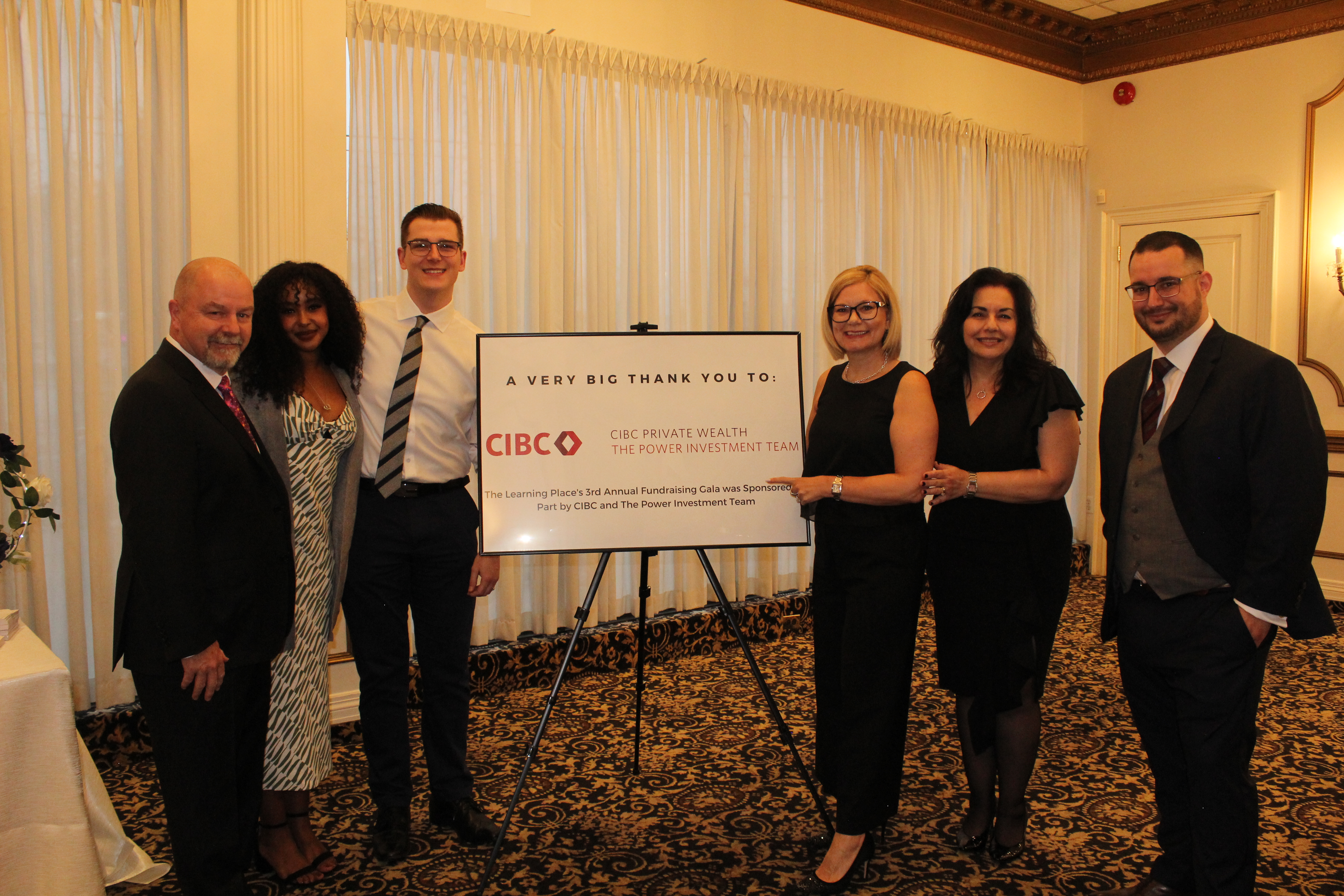 The Power Investment Team group photo beside sponsorship sign at The Learning Place Gala in April 2023